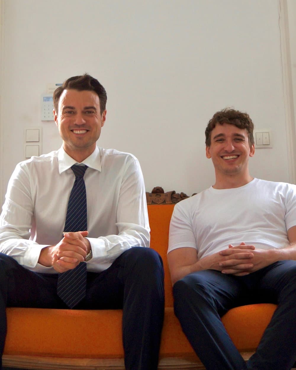 Johannes Freyer and Torben Lange laughing side by side on an orange sofa